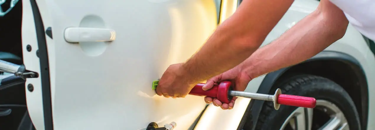 A technician pulling a small dent out of a car door